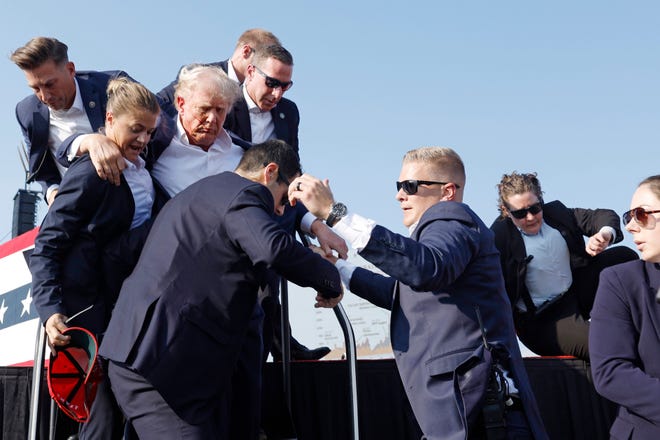 A Secret Service officer holds the red "Make America Great Again" baseball cap Trump was wearing before the shots rang out as the team guide him down the stairs.