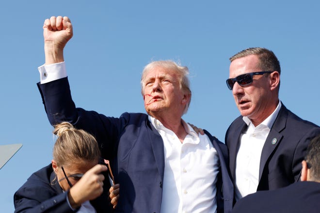 Republican presidential candidate and former President Donald Trump raised his fist to the air as Secret Service officers guide him off the stage.