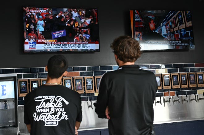 People in a bar outside the Fiserv Forum in Milwaukee, Wisconsin, watch the news after hearing that Donald Trump was evacuated from the rally in Pennsylvania.