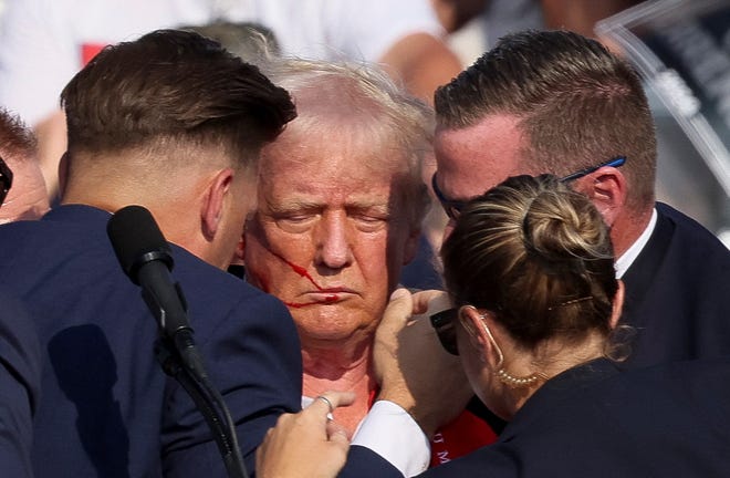 Still surrounding the former president, Secret Service officers helped Trump up, with blood on his ear and face visible.