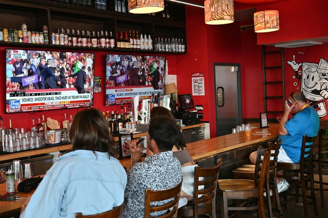 People watch the news on television inside a bar on July 13, 2024, in Milwaukee, Wisconsin, after hearing that Donald Trump was evacuated from the stage of his rally in Pennsylvania after shots were fired.