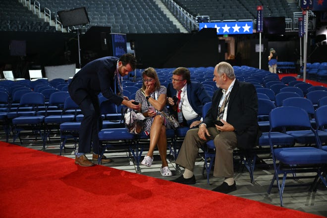 People inside the Fiserv Forum in Milwaukee, Wisconsin, watch the news on their phone after hearing that Donald Trump was evacuated from the stage of his rally in Pennsylvania.